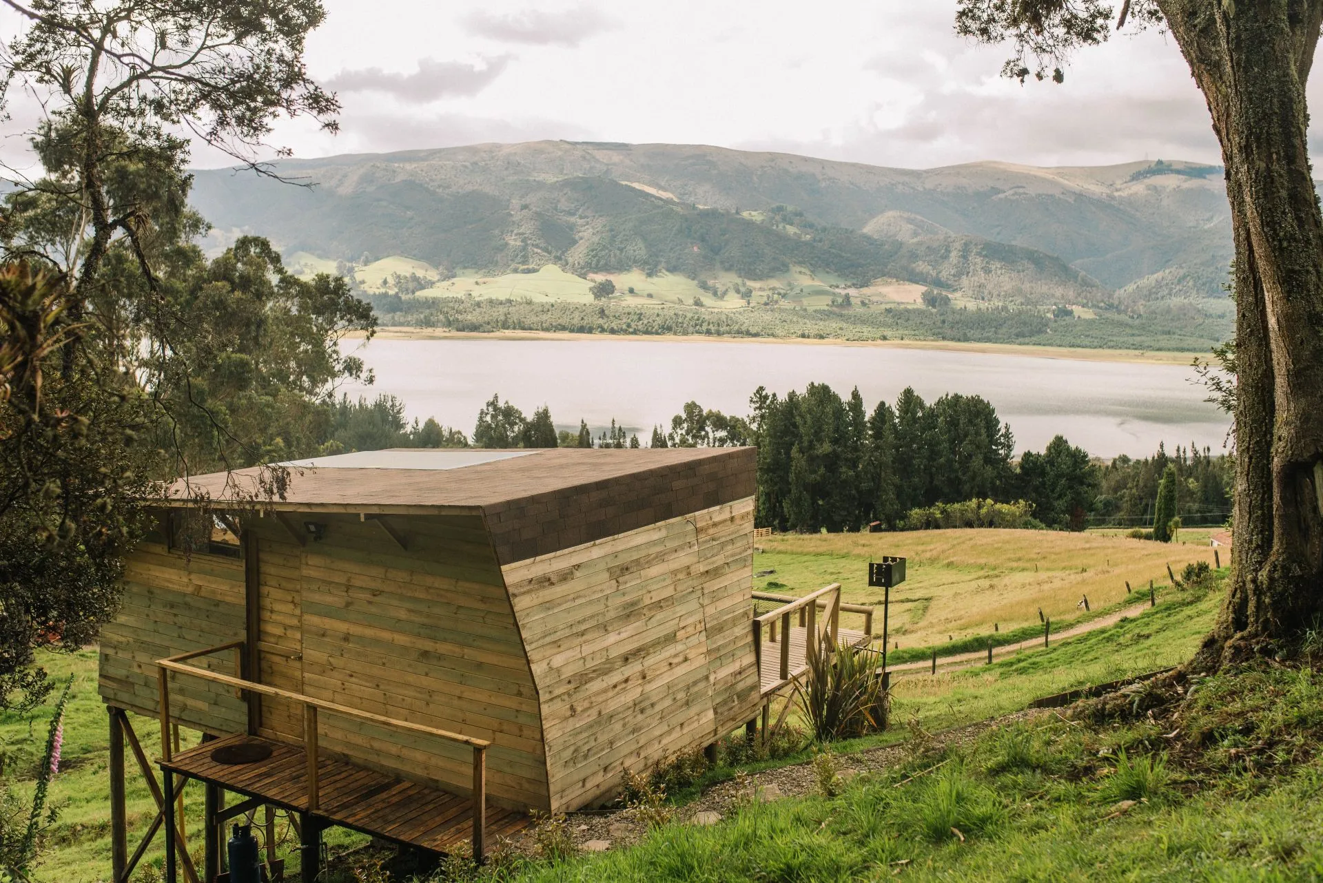 Cabaña de madera de Neusa Hills en una ladera, con el embalse del Neusa y montañas verdes al fondo