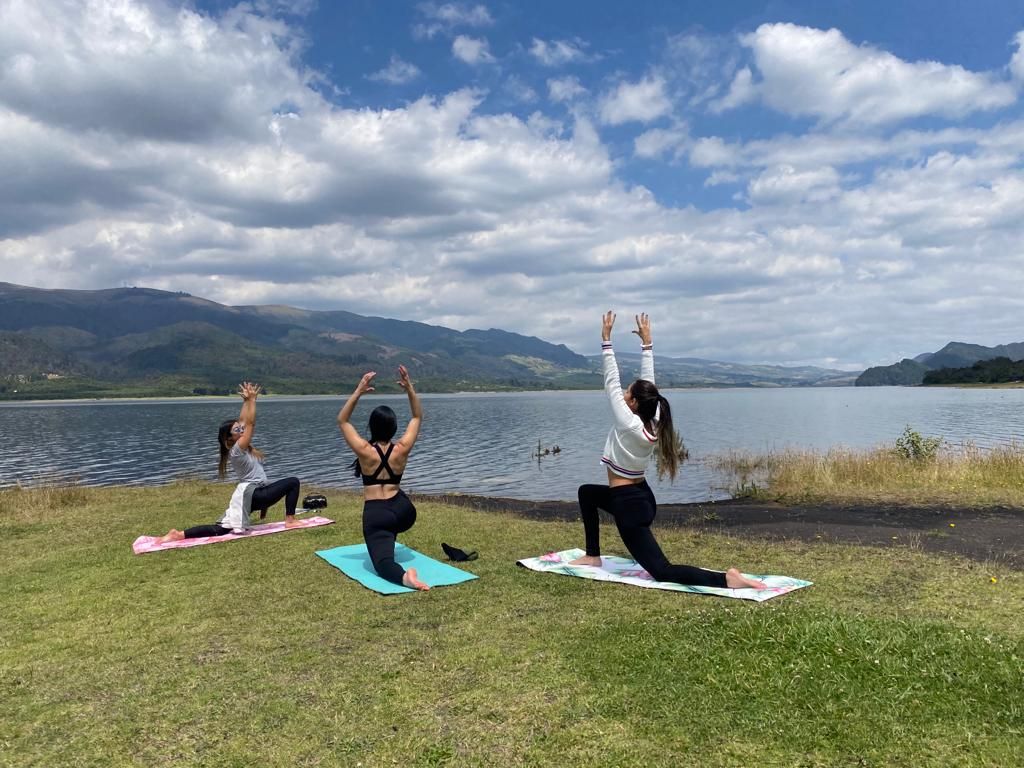 Three women practicing yoga on the lawn beside the Neusa reservoir