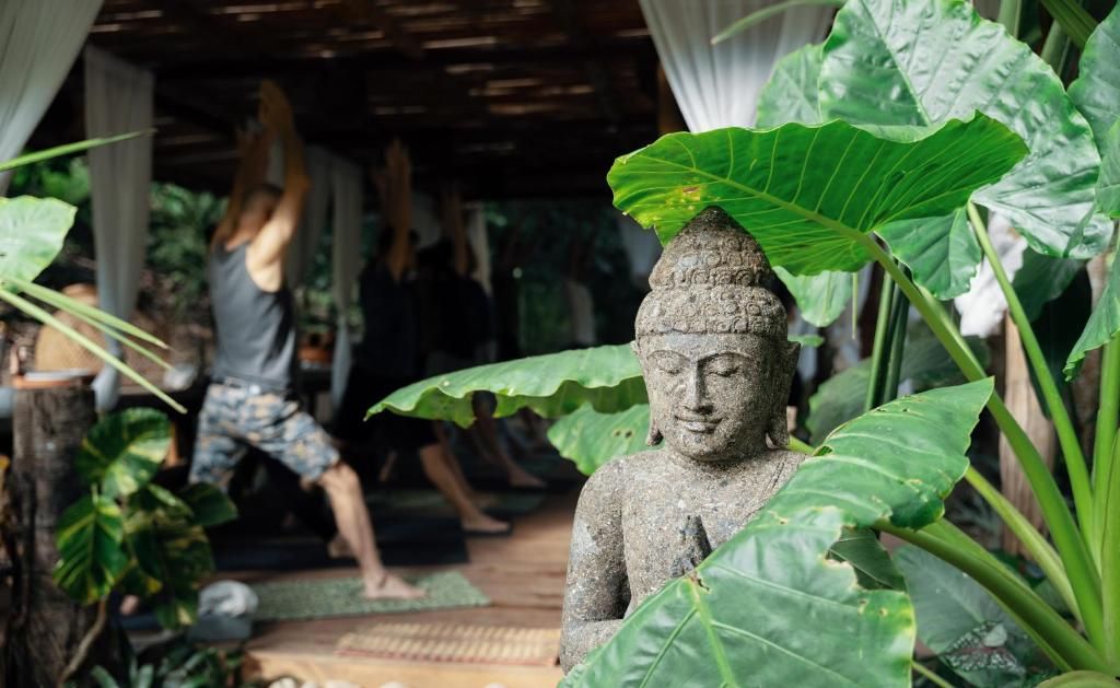 Yoga class indoors at One Santuario, with a stone Buddha statue and large tropical leaves in the foreground