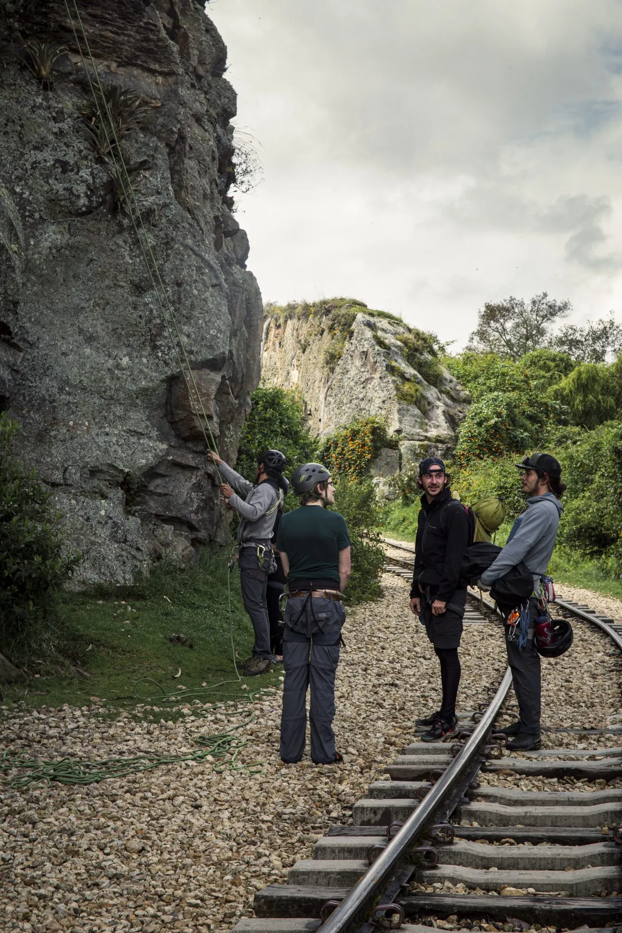 Climbers with helmets and harnesses at the foot of a rock face beside the railway line at Suesca, one of them handling a rope